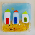 Decorative glass coaster with beach huts on a sandy beach with the sun shining.