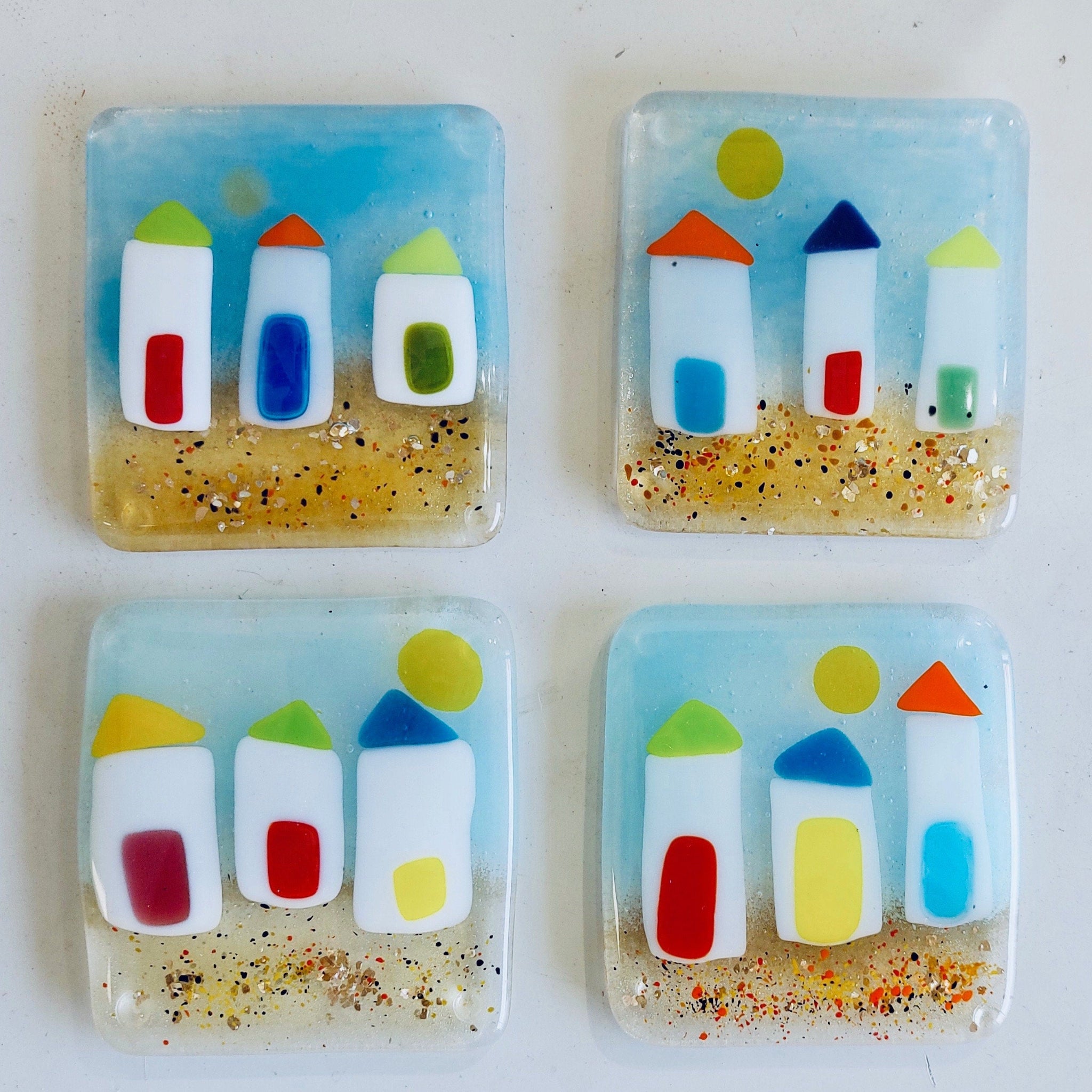 Four square glass coasters with colorful beach hut design on a white background